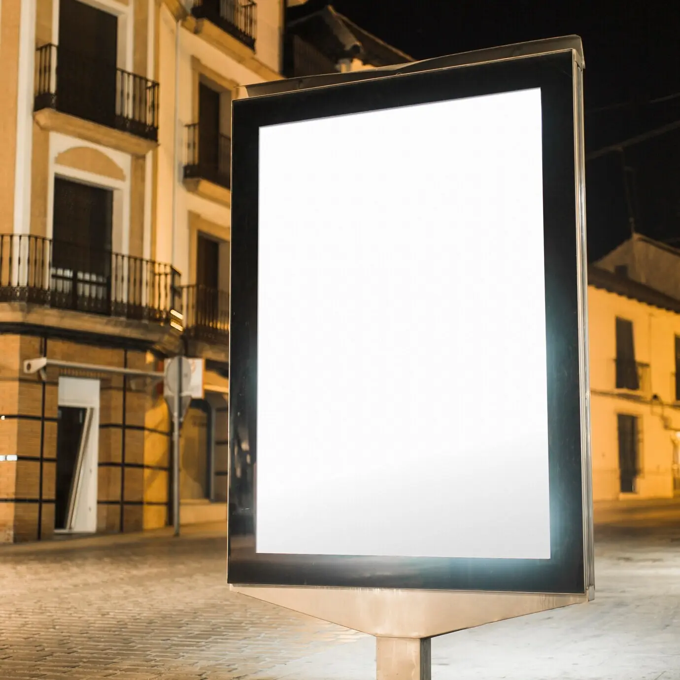 Unbeschriftete, beleuchtete, hochformatige Plakatwand bei Nacht.